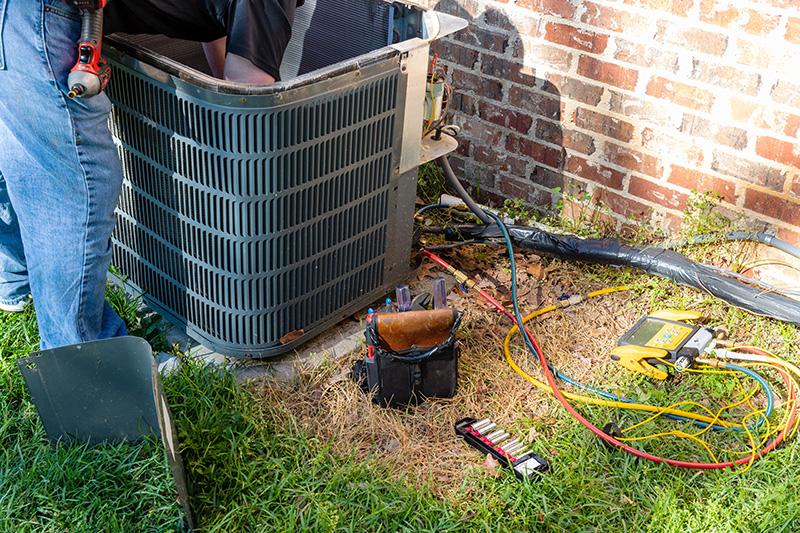 HVAC technician repairing an outdoor air conditioning condenser unit at a residential home