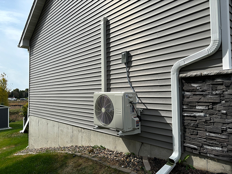 Outdoor ductless mini-split condenser installed on the side of a residential home